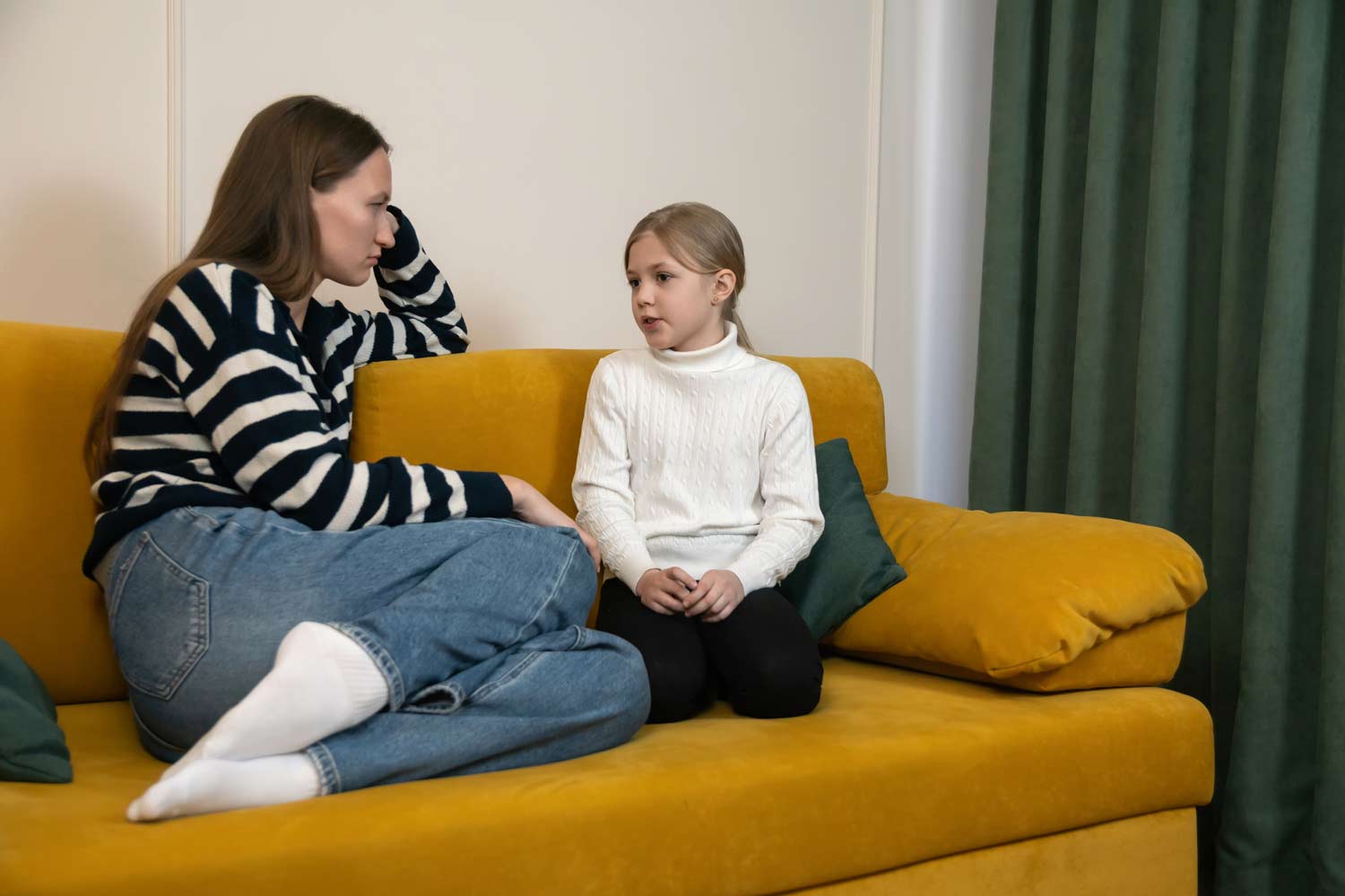 Parent and young child sitting together on a couch having a calm conversation, representing positive parenting, child therapy, emotional support, and healthy family communication.