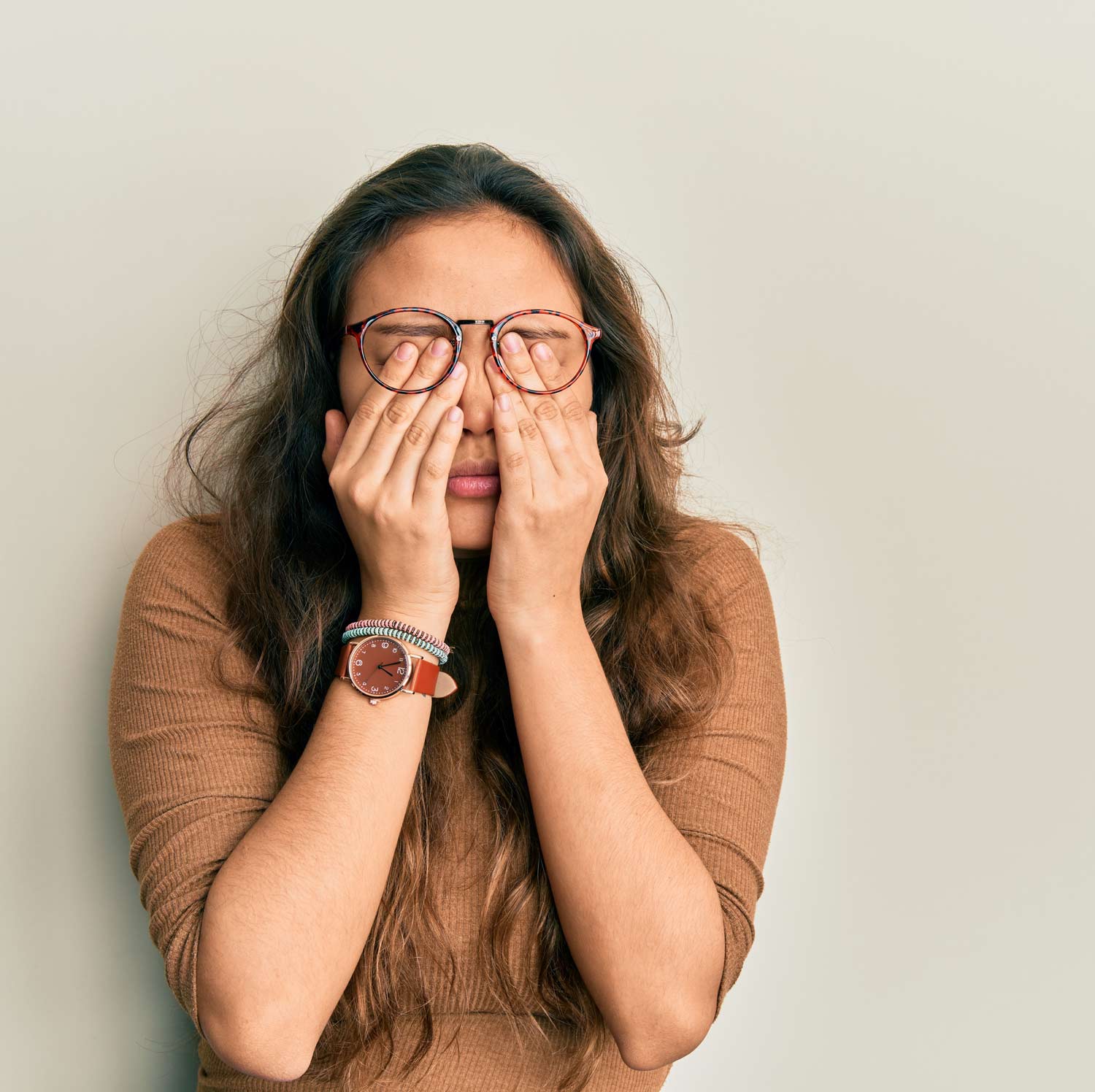 Person covering their eyes with both hands while wearing glasses, illustrating stress, emotional exhaustion, burnout, anxiety, or mental health challenges.
