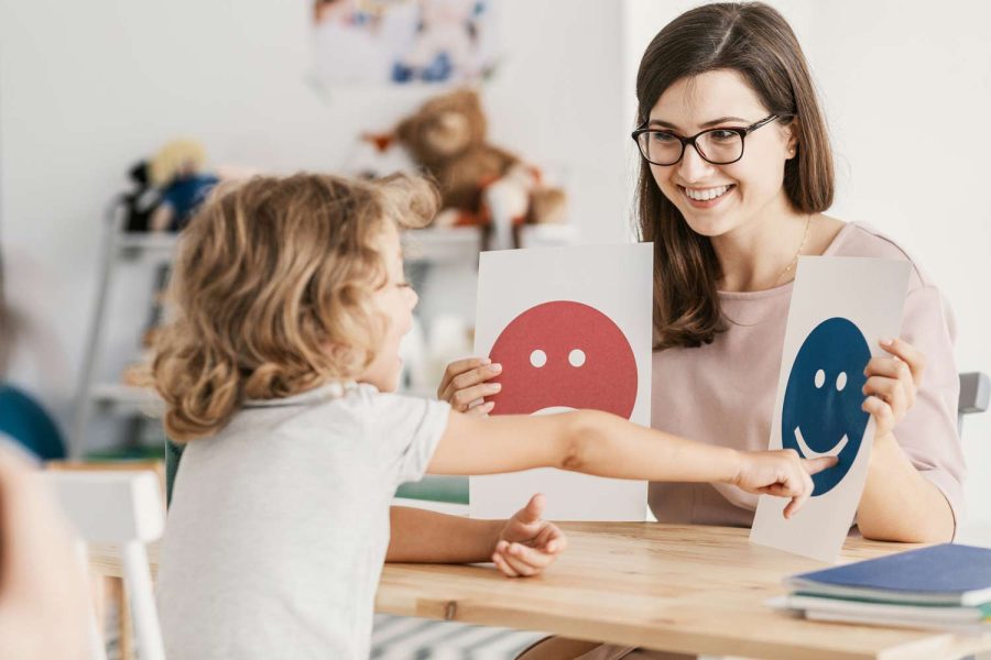 Child pointing to emotion cards with a therapist during a behavioral therapy session, helping develop emotional awareness, coping skills, and social-emotional development.
