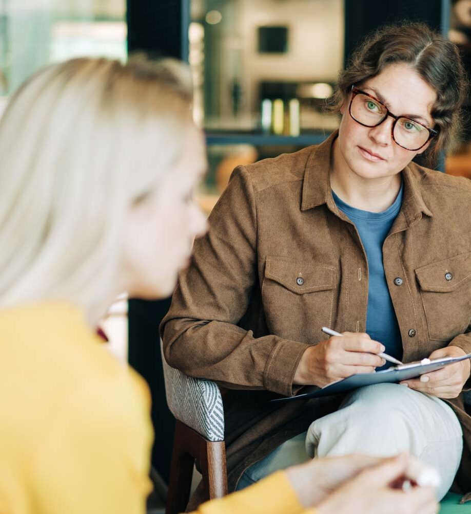 Licensed therapist taking notes while listening to a client during an individual counseling session focused on mental health and emotional well-being.