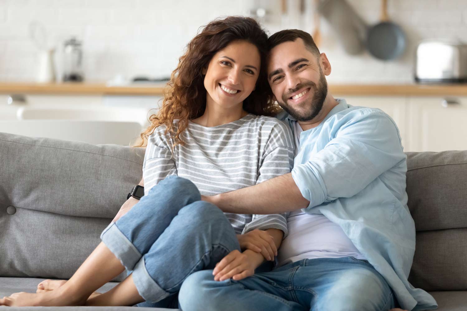 Smiling couple sitting together on a couch at home, representing healthy relationships, emotional connection, couples therapy, and premarital counseling.