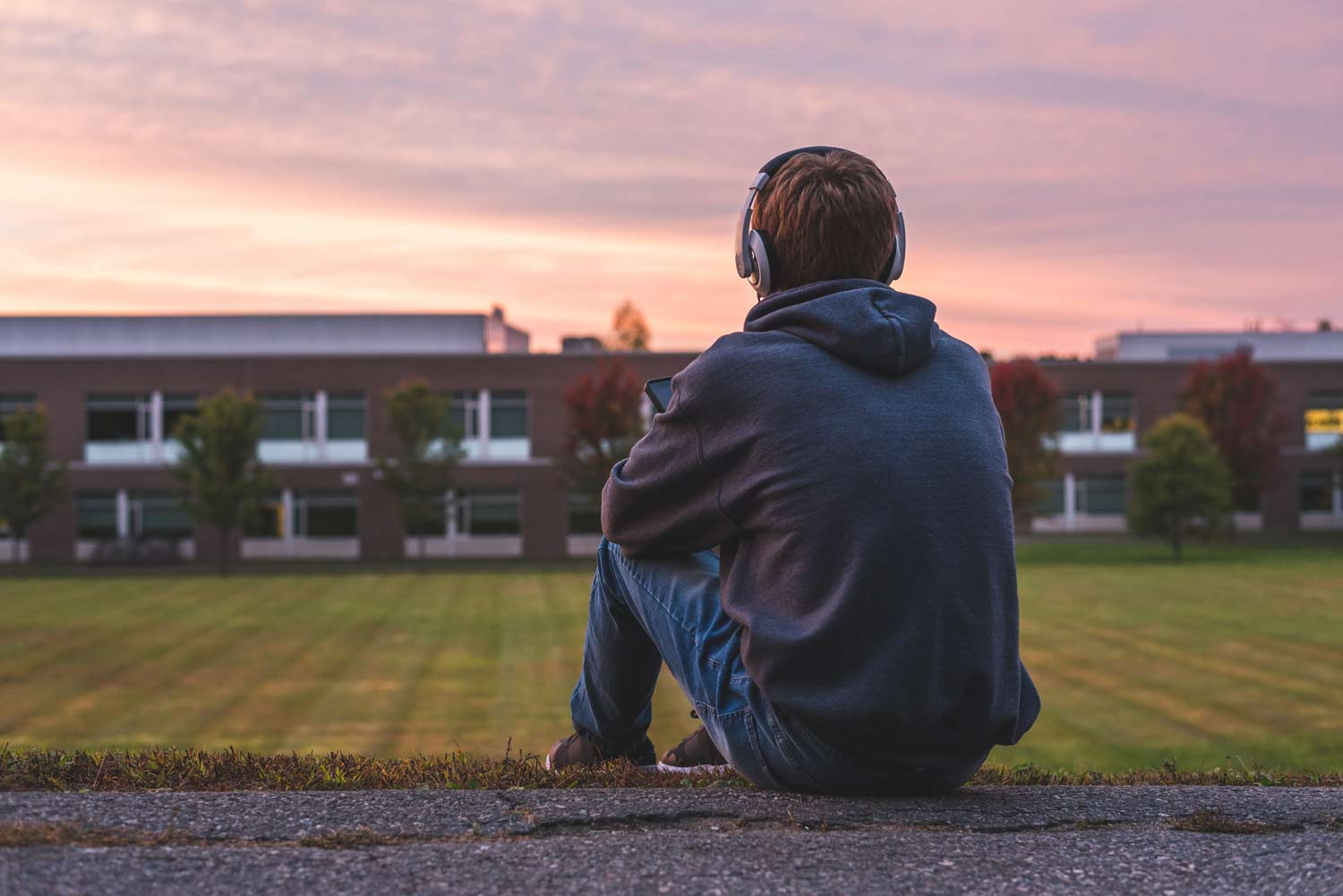 Teen sitting alone outdoors wearing headphones at sunset, representing adolescent depression, social isolation, emotional struggles, and teen mental health.